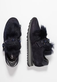 Navy suede shoes with faux fur accents, decorative blue beads, and a textured sole. Features a buckle and a low-profile design.