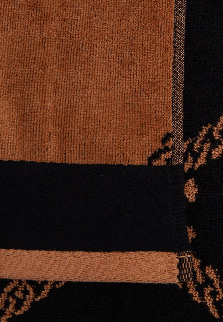 Zwart en bruin geweven textiel met een gestructureerd oppervlak, gekenmerkt door een onderscheidend patroon en contrasterende horizontale strepen aan de randen.