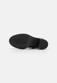 Suela de zapato negra con goma texturizada, que presenta surcos para agarre y un borde redondeado suave. La base es plana con una ligera curva en la zona del talón.