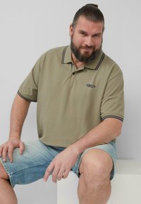 Khaki poloshirt met marineblauwe accenten, voorzien van een klassieke kraag en korte mouwen, gecombineerd met vervaagde denimshorts.