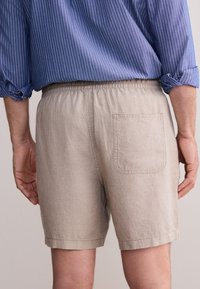 Pantaloncini beige chiaro con vita elastica e una tasca posteriore. Realizzati in tessuto strutturato, presentano un taglio semplice e dritto.