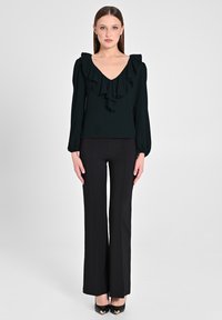 Blusa nera con scollo a V e colletto arricciato, abbinata a pantaloni neri aderenti e tacchi chiusi. Tessuto liscio, design strutturato.