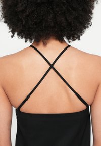 Fekete ujjatlan ruha keresztpántokkal és gombos részlettel, sima textúrával és testhez simuló sziluettel.