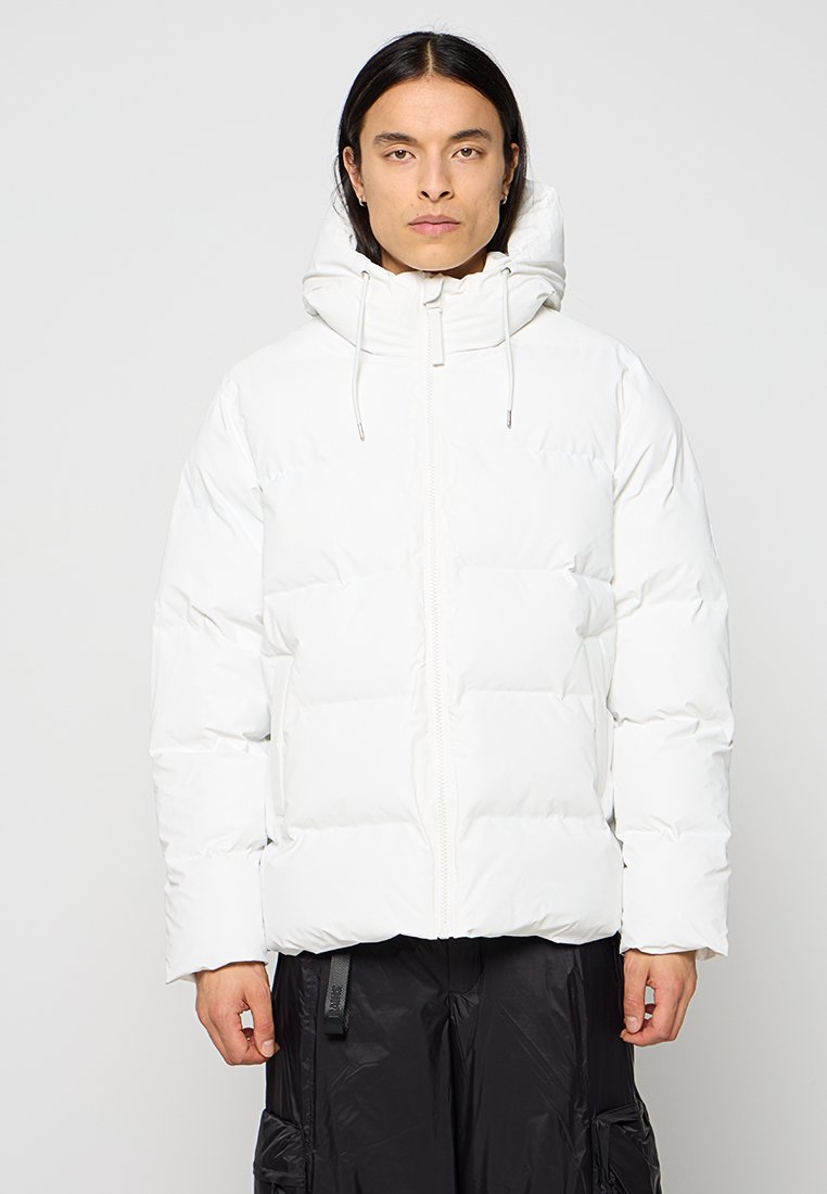 Veste blanche rembourrée avec une fermeture éclair sur le devant, une capuche et des cordons de serrage. Elle présente une coupe carrée et une texture lisse, associée à un pantalon noir.
