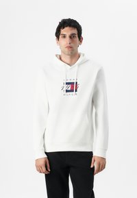 Weißer Kapuzenpullover aus Baumwolle mit einer Front-Kängurutasche, ausgestattet mit einem bunt bedruckten Tommy Hilfiger-Logo auf der Brust.