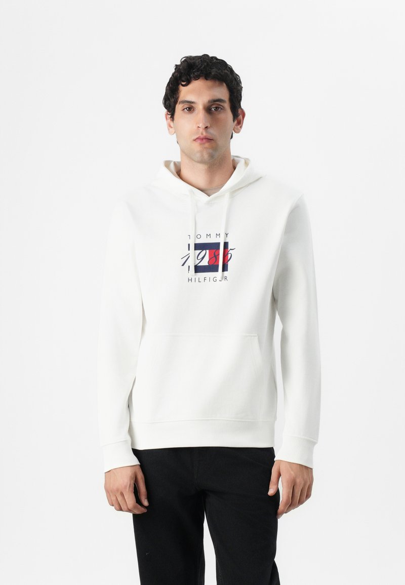 Weißer Kapuzenpullover aus Baumwolle mit einer Front-Kängurutasche, ausgestattet mit einem bunt bedruckten Tommy Hilfiger-Logo auf der Brust.