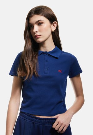 Polo in blu navy con colletto, maniche corte, tre bottoni e un logo rosso sul lato sinistro del petto. Tessuto in cotone liscio.