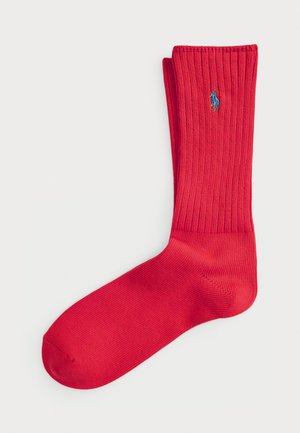 Raudonos storos kojinės su vientisu tekstūru, šone siuvinėtas mažas mėlynas logotipas. Standartinio ilgumo dizainas.