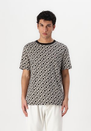 T-shirt z krótkim rękawem w kolorze czarnym i kremowym, z misternym wzorem geometrycznym oraz prążkowanym czarnym dekoltem. Materiał ma gładką fakturę.