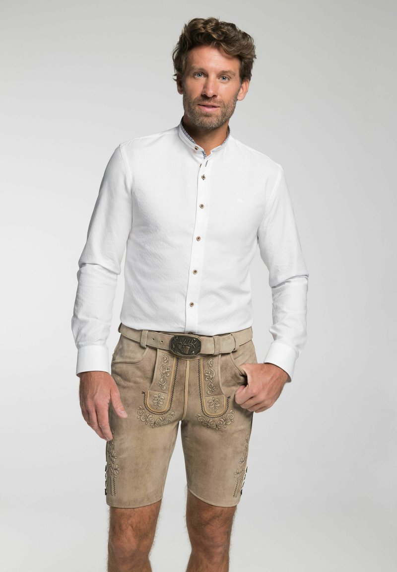 Weißes Hemd mit strukturiertem Stoff, kombiniert mit tanfarbenen Lederhosen, die mit gestickten Blumenmustern und einer dekorativen Gürtelschnalle verziert sind.