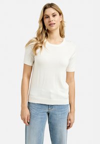 Weißes kurzärmliges Strickoberteil mit rundem Halsausschnitt, glatter Textur und taillierter Passform, kombiniert mit hellblauen Jeans.