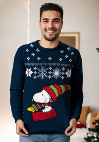 Maglione lavorato a maglia blu navy con fiocchi di neve bianchi e una grafica di Snoopy che indossa un cappello a strisce rosso e verde, mentre tiene un oggetto giallo.