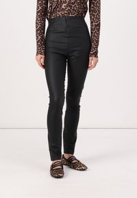 Svarta högmidjade byxor i konstläder med en slät yta, med en dragkedja fram. Tillsammans med en topp i brun och svart leopardmönster samt skor.