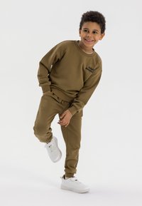 Olijfgroen sweat-outfit met een crewneck sweatshirt en bijpassende broek, met de tekst "totally awesome", gecombineerd met witte sneakers.