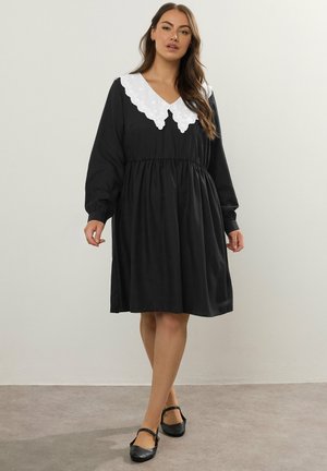 Robe noire à manches longues, avec un col blanc à bords festonnés et une taille froncée. Dotée d'une coupe décontractée et d'une texture lisse.