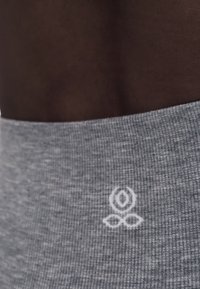 Κοντινό πλάνο σκούρου δέρματος και μέσης ατόμου που φορά γκρι ριμπ ύφασμα με μικρό λευκό λογότυπο λουλουδιού κοντά στη μέση.