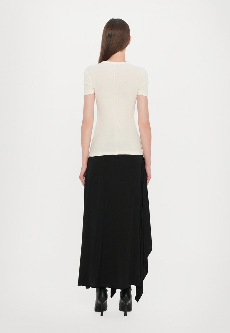 Top corto de manga corta en color crema combinado con una falda maxi negra. La falda tiene un diseño drapeado, llegando por debajo de la rodilla, con calzado de tacón.