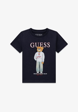 T-shirt noir avec le texte « GUESS » au-dessus d'un ours portant un sweat à capuche blanc et un jean, avec « Original Authentic Brand Est. 1981 » en dessous.