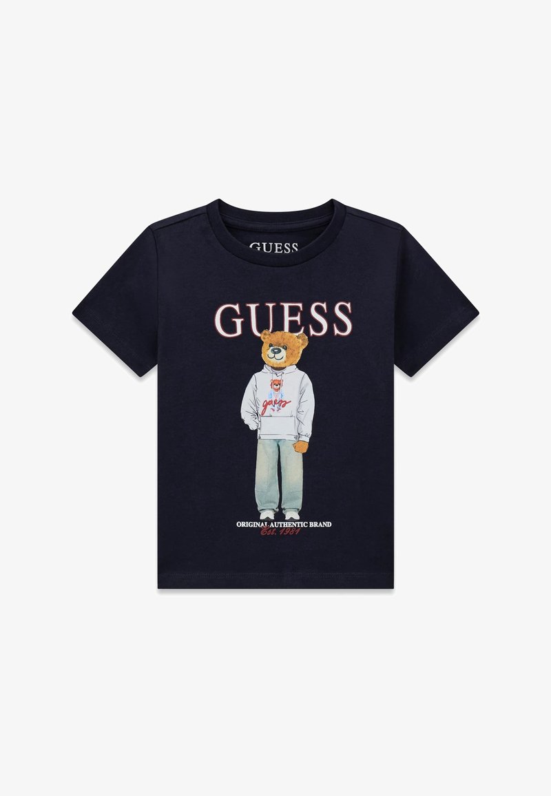 T-shirt noir avec le texte « GUESS » au-dessus d'un ours portant un sweat à capuche blanc et un jean, avec « Original Authentic Brand Est. 1981 » en dessous.