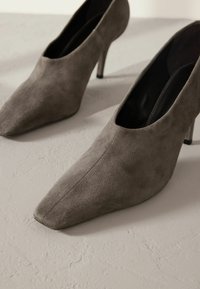 Chaussures à talons hauts en suède gris avec un design à bout pointu, présentant une texture lisse et une silhouette élégante. Détails de talon stiletto visibles.