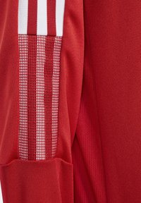 Camiseta atlética roja con tejido texturizado, paneles de malla con rayas verticales y acentos blancos contrastantes a lo largo de las mangas.