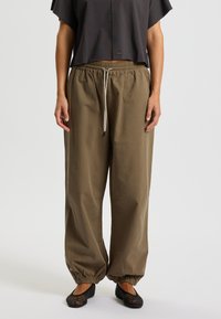 Housut, joissa on löysä istuvuus, khaki-väriset, joustava vyötärö ja nauhakuja, säädettävät lahkeensuut. Yhdistetty tumman väriseen lyhythihaiseen toppiin ja mustiin kengiin.