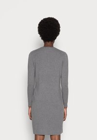 Abito grigio lavorato a maglia con maniche lunghe, scollatura a girocollo e silhouette aderente, che si estende fino a metà coscia con spacchi laterali per facilitare i movimenti.
