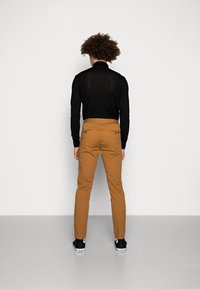 Černá košile s dlouhým rukávem v kombinaci s béžovými úzkými kalhotami. Viditelné zadní kapsy a poutka na pásek. Černé tenisky s bílými detaily.