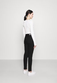 Calças pretas com um corte slim, cintura média, e detalhes em costura branca, combinadas com uma blusa justa de manga longa canelada branca e ténis brancos.