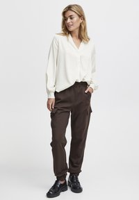 Crème blouse met een V-hals en pofmouwen, gecombineerd met donkerbruin cargo-broek met elastische tailleband, zijzakken en taps toelopende manchetten.