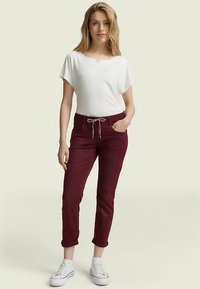 Biały top z krótkim rękawem i okrągłym dekoltem, w zestawie z bordowymi, zwężanymi spodniami z troczkiem w pasie i podwiniętymi nogawkami. Białe trampki.