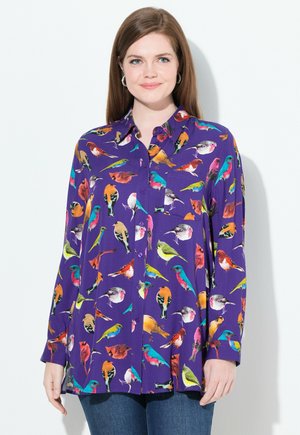 Chemise violette à boutons avec un imprimé d'oiseaux colorés, à manches longues et coupe décontractée. Le tissu semble lisse avec une texture légère.