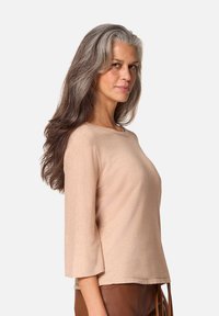 Beige, langmouw top met een ronde halslijn en driekwart mouwen, gemaakt van een zachte, textuurstof. Eenvoudig ontwerp zonder patronen of accenten.