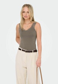 Olivenfarvet tanktop med blonderkant, parret med lysebeige højhalsede bukser og et brunt bælte, holdt med et brunt rem.