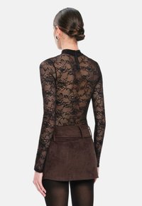 Zwarte kant bodysuit met lange mouwen, bloemenpatroon, hoge hals en sluiting aan de achterkant, gecombineerd met een bruine suede mini-rok.