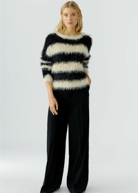 Pull rayé flou en crème et noir, avec un large col et des manches trois-quarts, associé à un pantalon noir à taille haute et jambes larges.