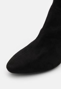 Nahaufnahme eines schwarzen, spitz zulaufenden Stiefeletten aus Wildleder mit sichtbaren Nähten am oberen Teil.