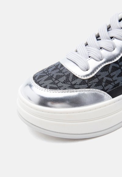 Κοντινό πλάνο μύτης αθλητικού παπουτσιού με μεταλλικές ασημί λεπτομέρειες, γκρι υφασμάτινο σχέδιο, λευκή παχιά σόλα και λευκά κορδόνια.