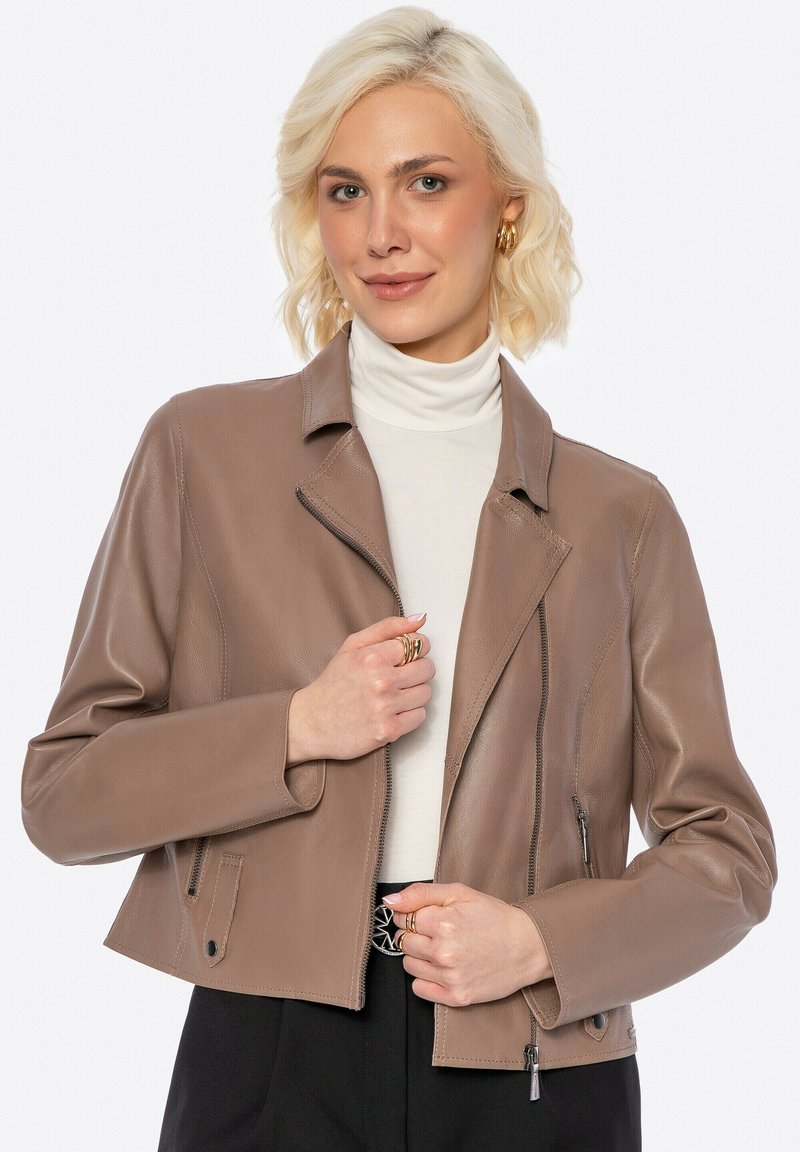 Bruine leren cropped jack met een uitgesneden kraag, asymmetrische ritssluiting en ritszakken. Gestyled over een witte coltrui.