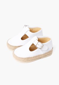 White canvas shoes with a T-strap design, beige espadrille-style jute sole, and a silver buckle detail. Smooth texture, rounded toe shape.