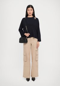 Woman with straight black hair wearing a loose black sweater, beige wide-leg cargo pants, black pointed shoes, and carrying a black crossbody bag.