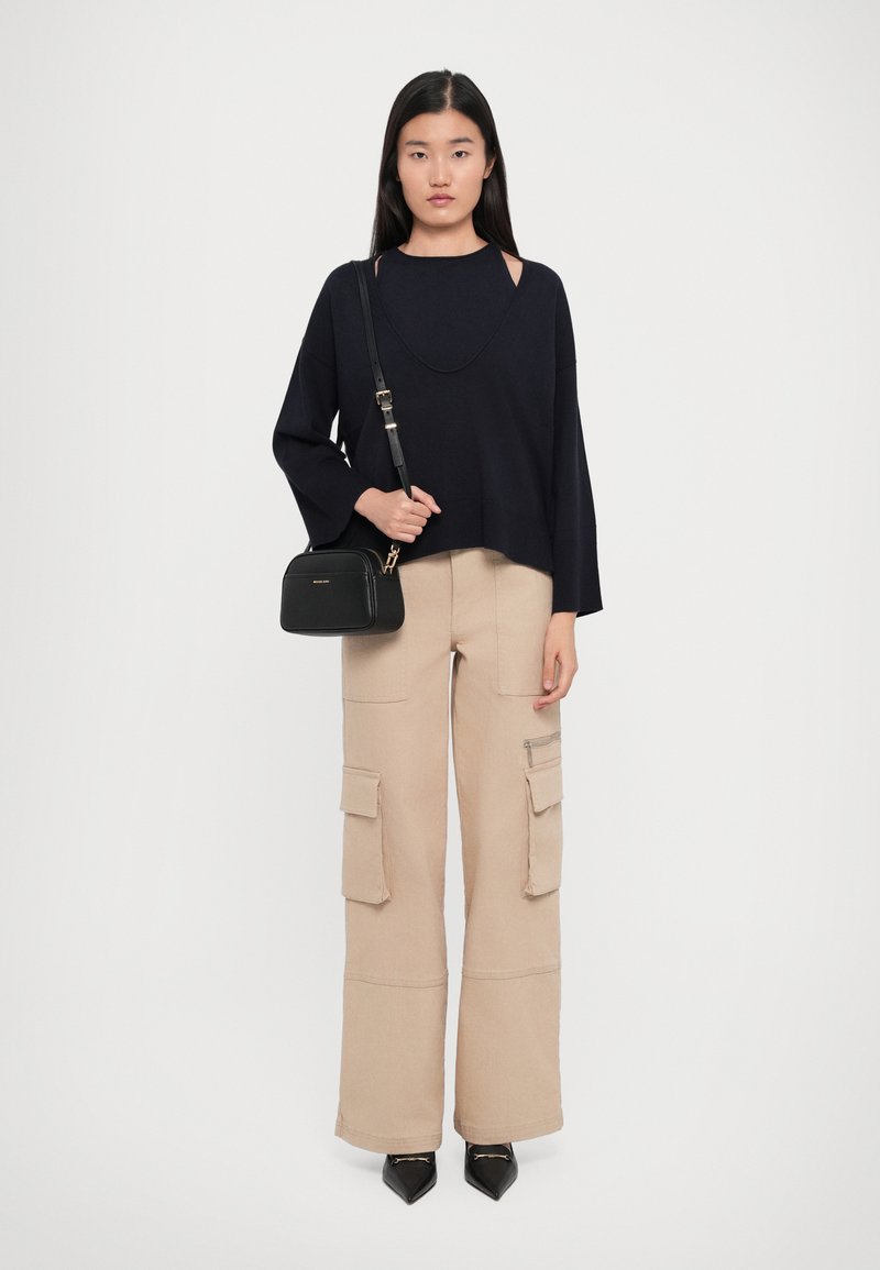 Woman with straight black hair wearing a loose black sweater, beige wide-leg cargo pants, black pointed shoes, and carrying a black crossbody bag.