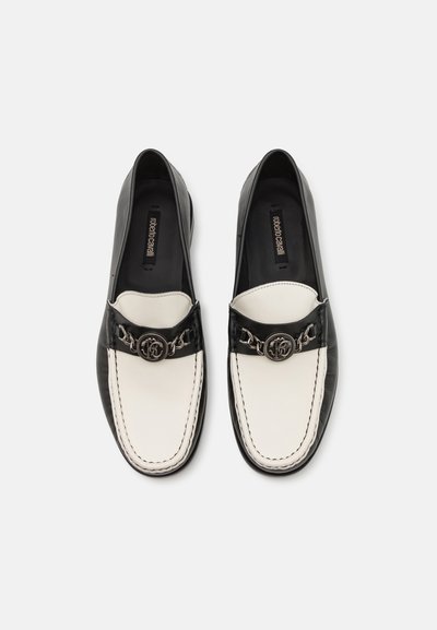 Black and white leather loafers with a stitched seam, metal chain accent, and logo detail on the upper. Smooth texture and slip-on design.