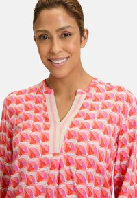 Tunica rosa con un motivo geometrico di foglie ripetuto in tonalità di rosa e rosso, con scollatura a V e una trama di tessuto morbido.