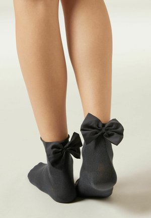 Chaussettes noires mi-mollet avec de grands nœuds en satin à l'arrière, dotées d'un matériau texturé et côtelé. Le design est simple et court.