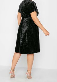 Černé sametové šaty s krátkými rukávy, rozšířenou sukní a zavazovacím páskem v pase. V kombinaci se stříbrnými sandály na vysokém podpatku.