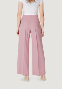 Pantaloni larghi rosa realizzati in tessuto morbido. Presentano pieghe frontali, una tasca posteriore e un logo del brand discreto vicino all'orlo della vita.