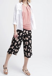 Biała koszula z guzikami, miękki różowy top z plisami, czarne kwiatowe culottes i brązowe klapki z akcentem w postaci paska. Gładkie faktury w całej stylizacji.