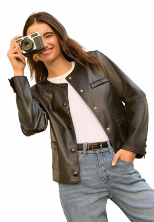 Black leather jacket with a snap-button closure, featured pockets, and a slightly fitted design. Worn over a white shirt and blue jeans.