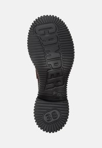 Czarna gumowa podeszwa z wyraźnymi żłobieniami, z wytłoczonym logo "CAMPER" oraz rozmiarem "38". Okrągłe wzory poprawiają przyczepność.